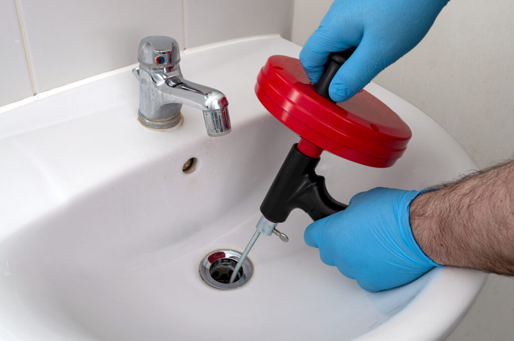 plumber repairing drain clog with plumbers snake (steel spiral that twists through pipes to collect dirt) in residential sink